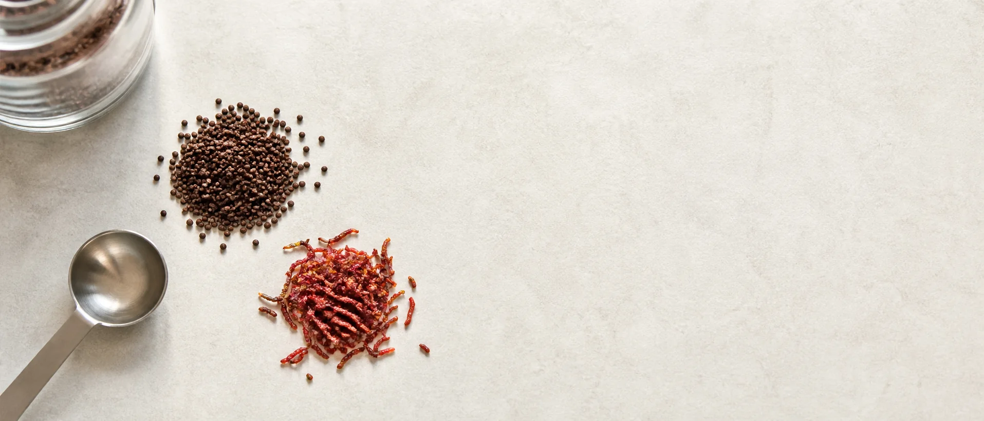 A small pile of betta pellets and frozen food beside a feeding spoon on a pale surface